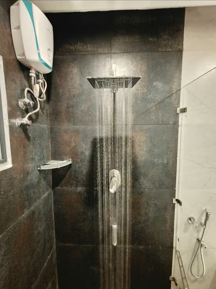 A walk-in shower with a rainfall head and instant water heater, tiled in dark stone