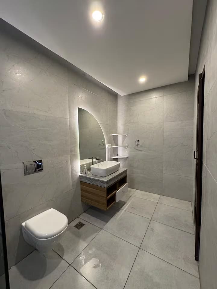 A wide view of the upstairs en-suite with wall-hung toilet, vanity and arched mirror