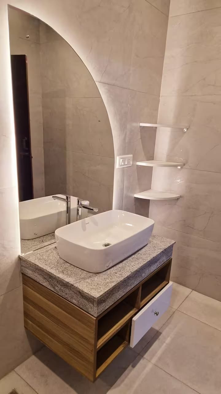 A vessel basin on a stone counter set into an arched alcove with corner shelving