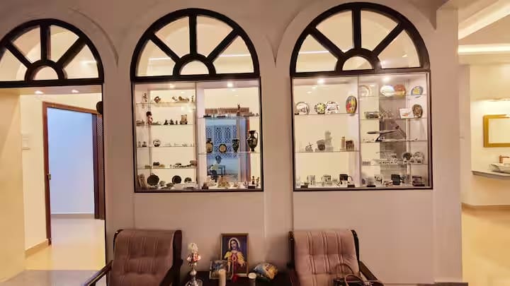 Glass display cabinets of collectables set between arched windows, with armchairs below
